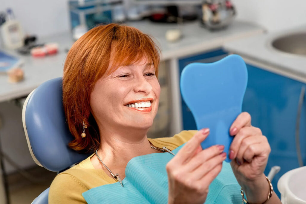 Smiling patient viewing her restored smile in a hand mirror