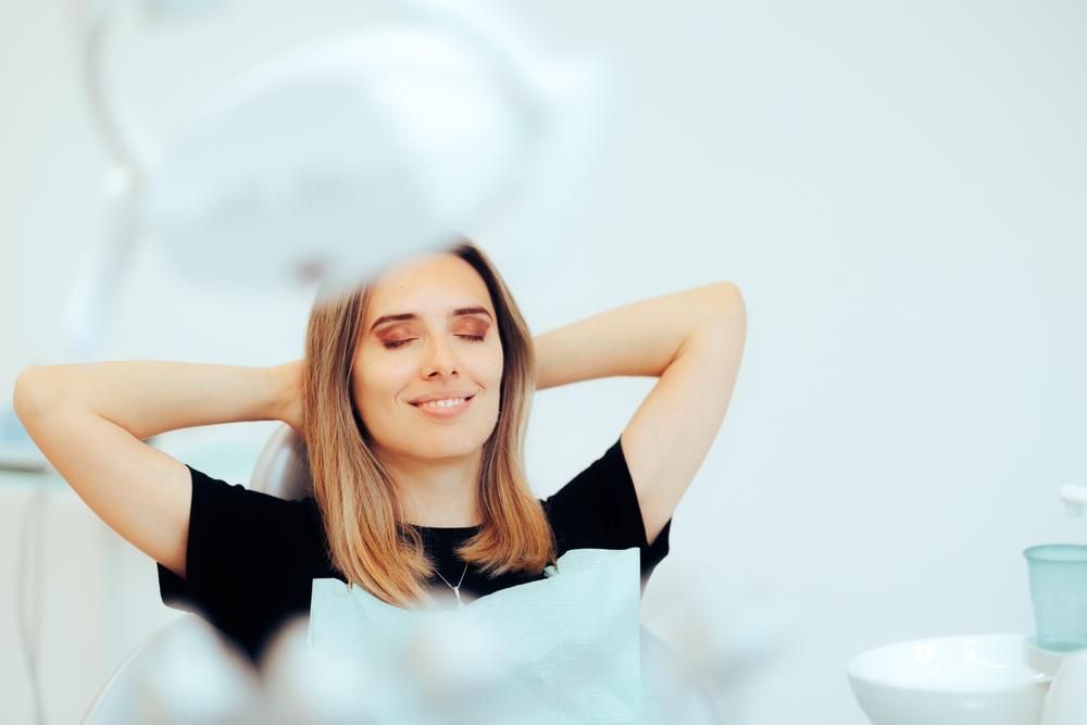 Image Alt Relaxed woman with closed eyes and hands behind her head in a dental chair.