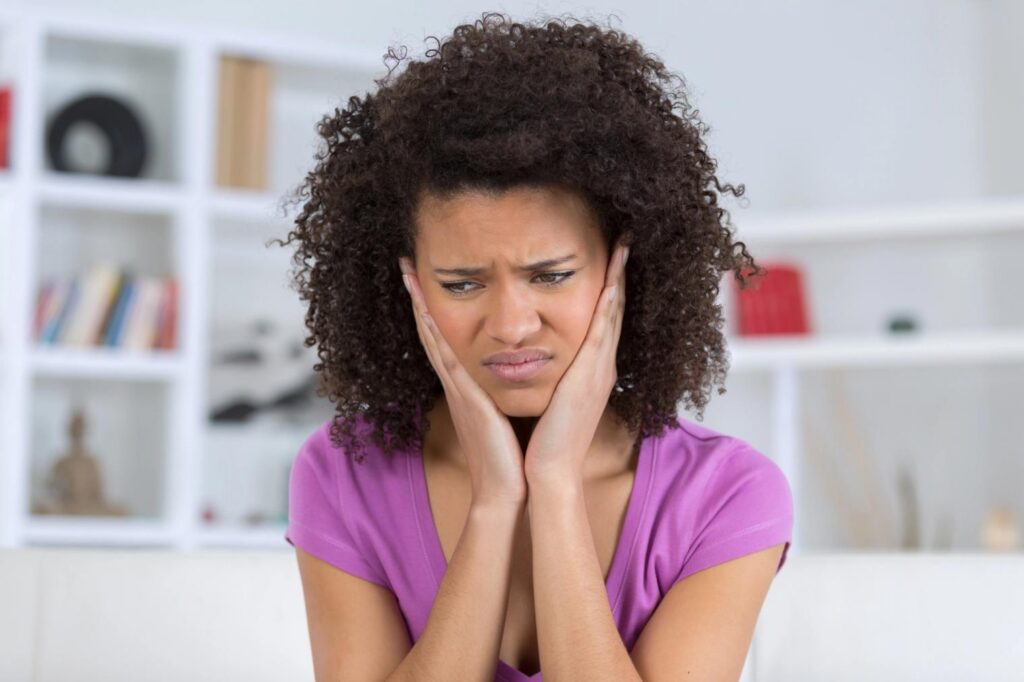 A woman with a pained expression holds her hands to her cheeks.