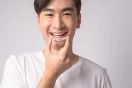 a young man is smiling while holding a clear brace on his teeth . a young man is smiling while holding a clear brace on his teeth .