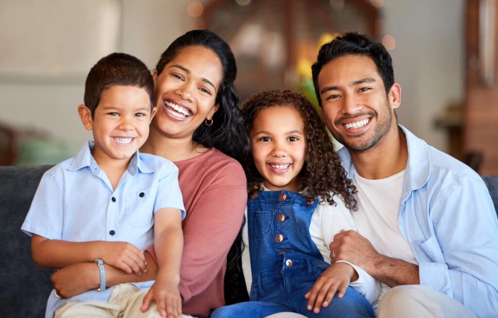 A smiling family of four, including a mother, father, son, and daughter, sitting together.