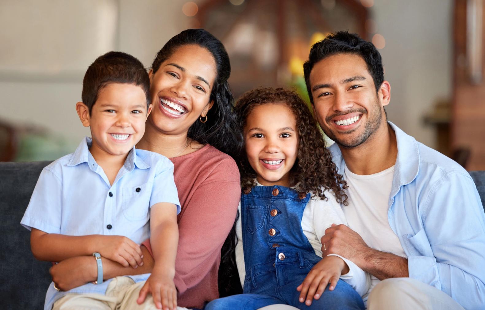 A smiling family of four, including a mother, father, son, and daughter, sitting together.