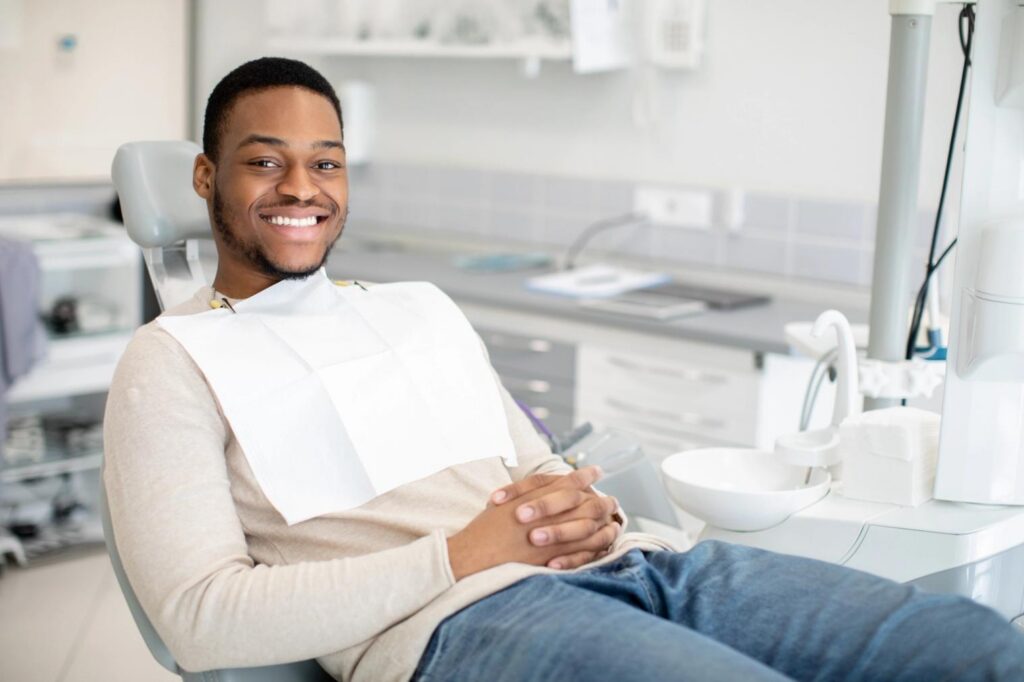 A young Black man with a dental bib smiles broadly in a dental chair.