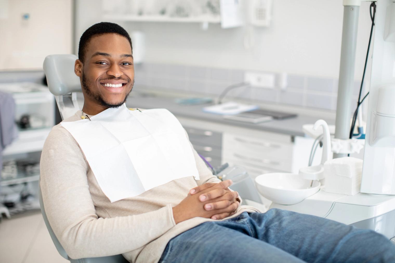 Image Alt A young Black man with a dental bib smiles broadly in a dental chair.