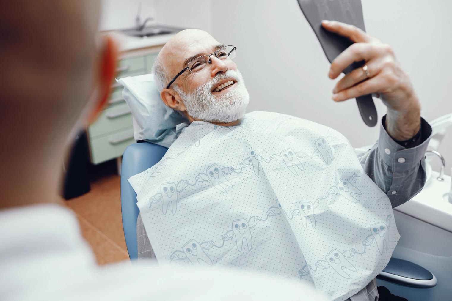 Image Alt an elderly man is sitting in a dental chair looking at his teeth in a mirror .