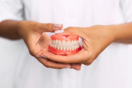 a woman is holding a denture in her hands . a woman is holding a denture in her hands .