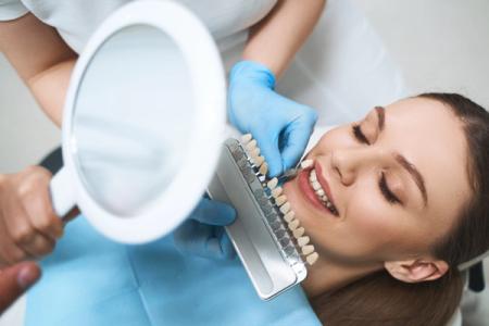 a woman is sitting in a dental chair while a dentist examines her teeth with a magnifying glass . a woman is sitting in a dental chair while a dentist examines her teeth with a magnifying glass .