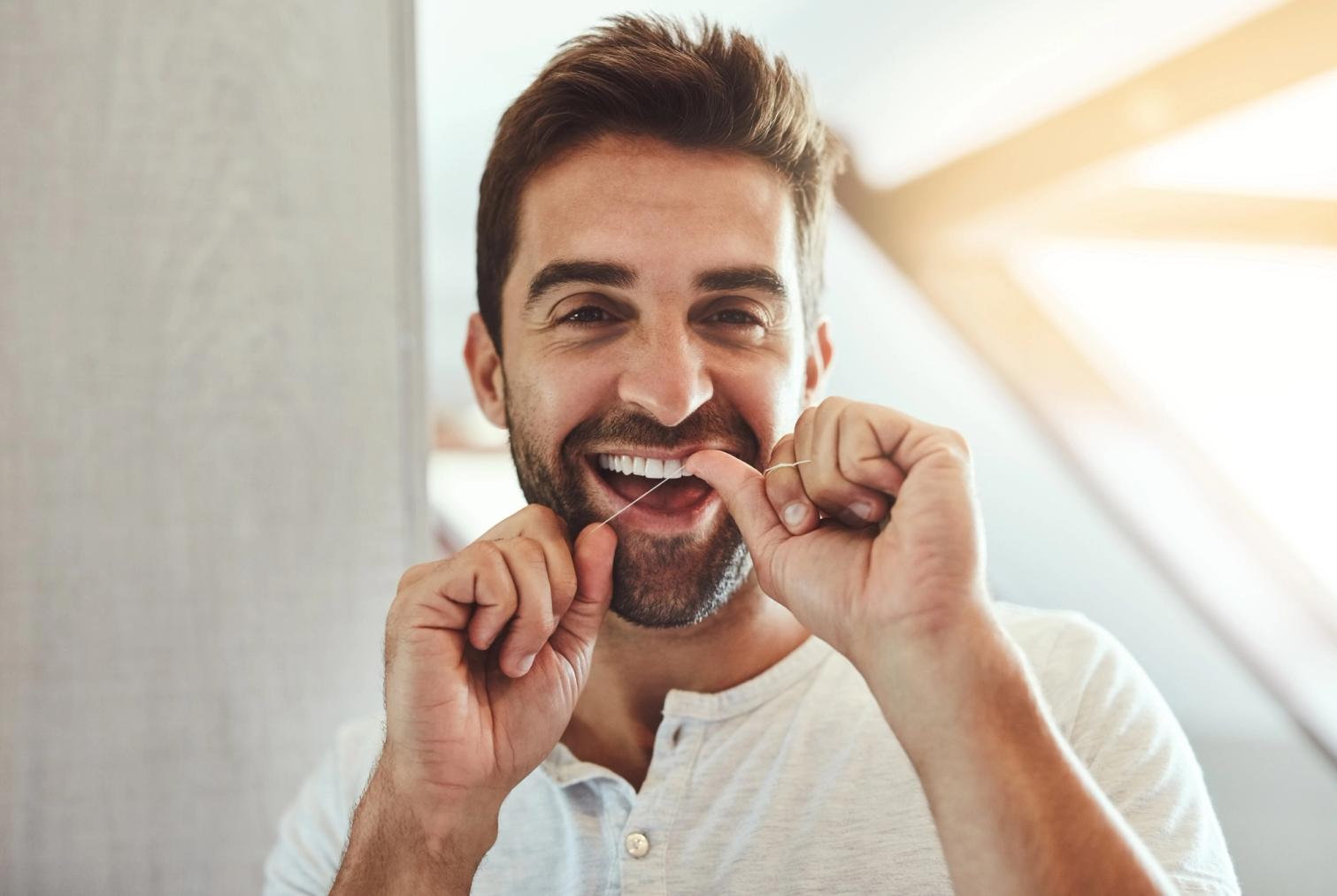 A smiling man flossing his teeth.