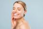Image Alt A smiling woman with closed eyes touches her cheek against a light blue background.