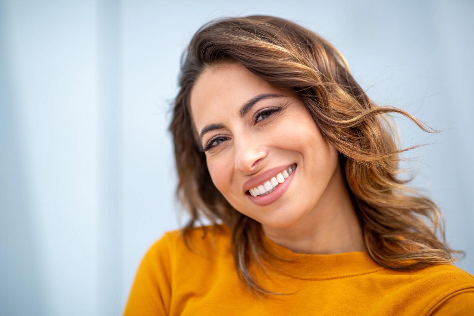 Image Alt Smiling woman with wavy brown hair in a mustard yellow top.