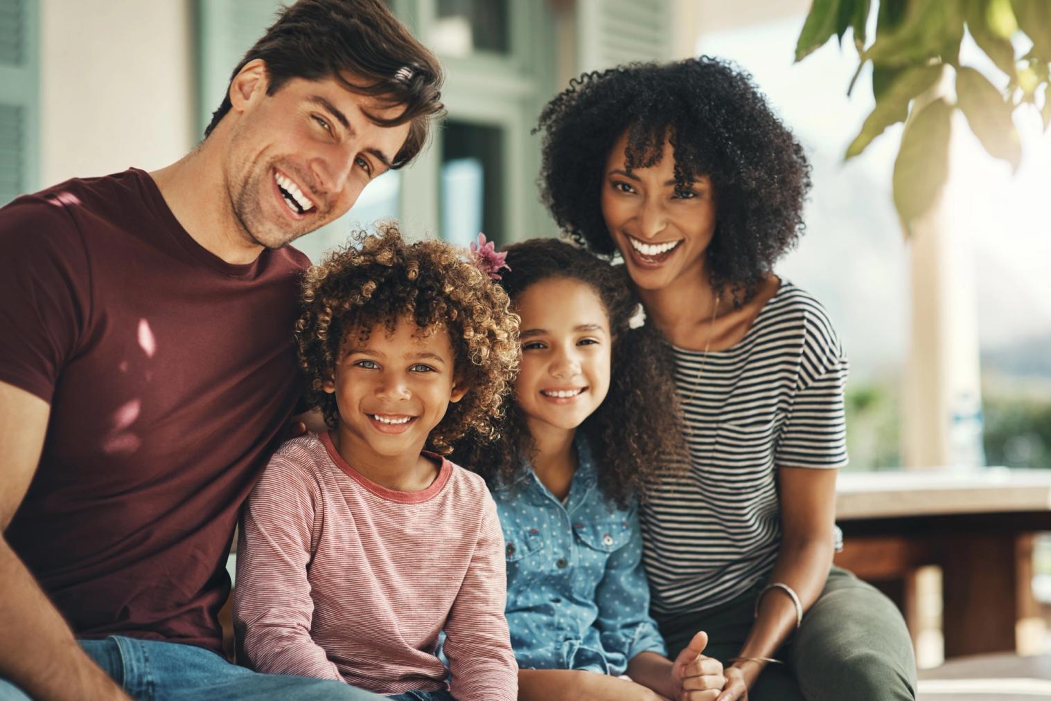 A smiling diverse family of four outdoors.