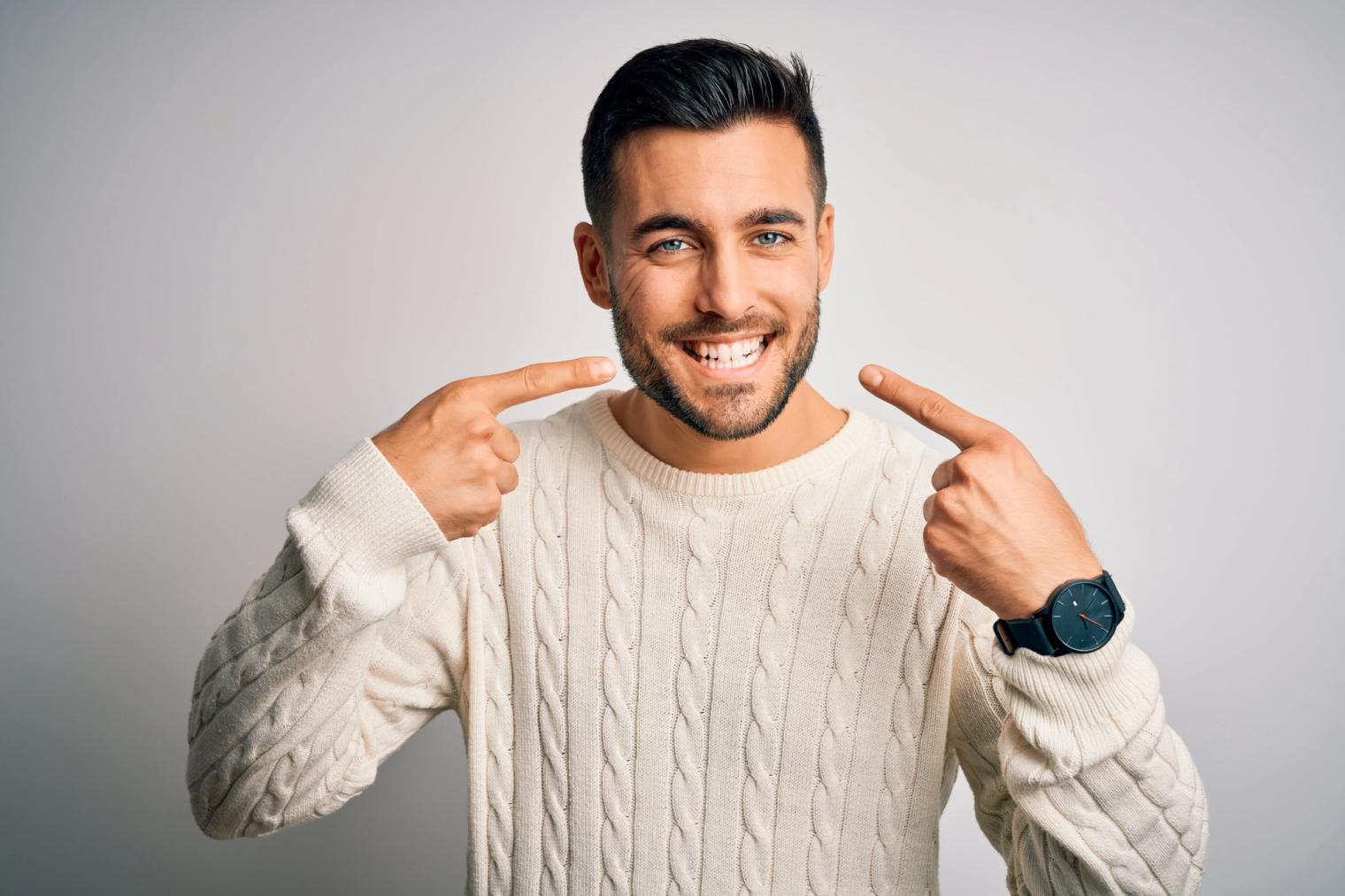 Image Alt A smiling man points to his white teeth.