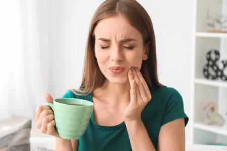 a woman is holding a cup of coffee and having a toothache . a woman is holding a cup of coffee and having a toothache .