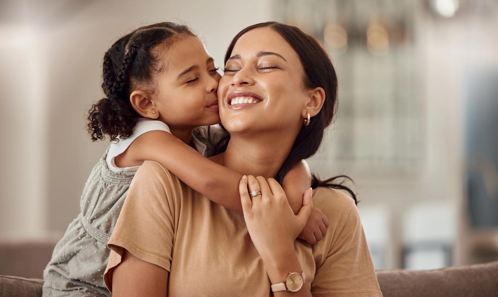 A young girl kisses a smiling woman on the cheek while hugging her.