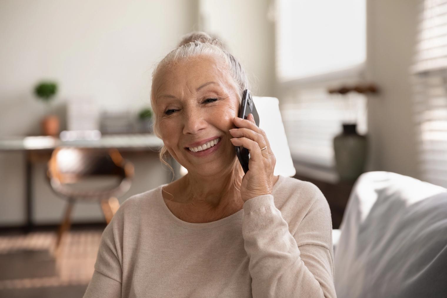 A smiling older woman talks on a smartphone.